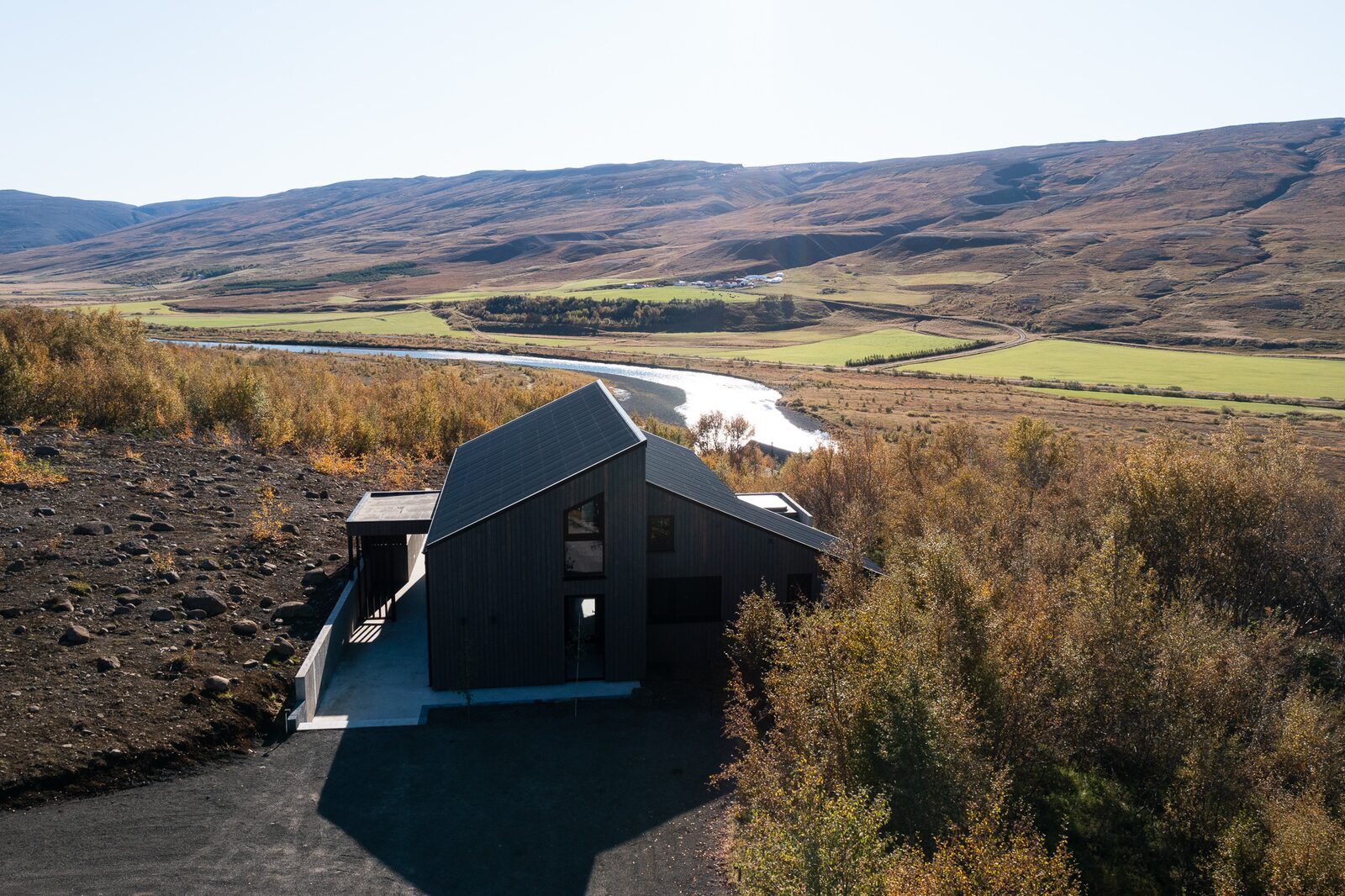 An aerial view of the dark timber house at Lundskógur surrounded by autumn colours in Fnjóskadalur.