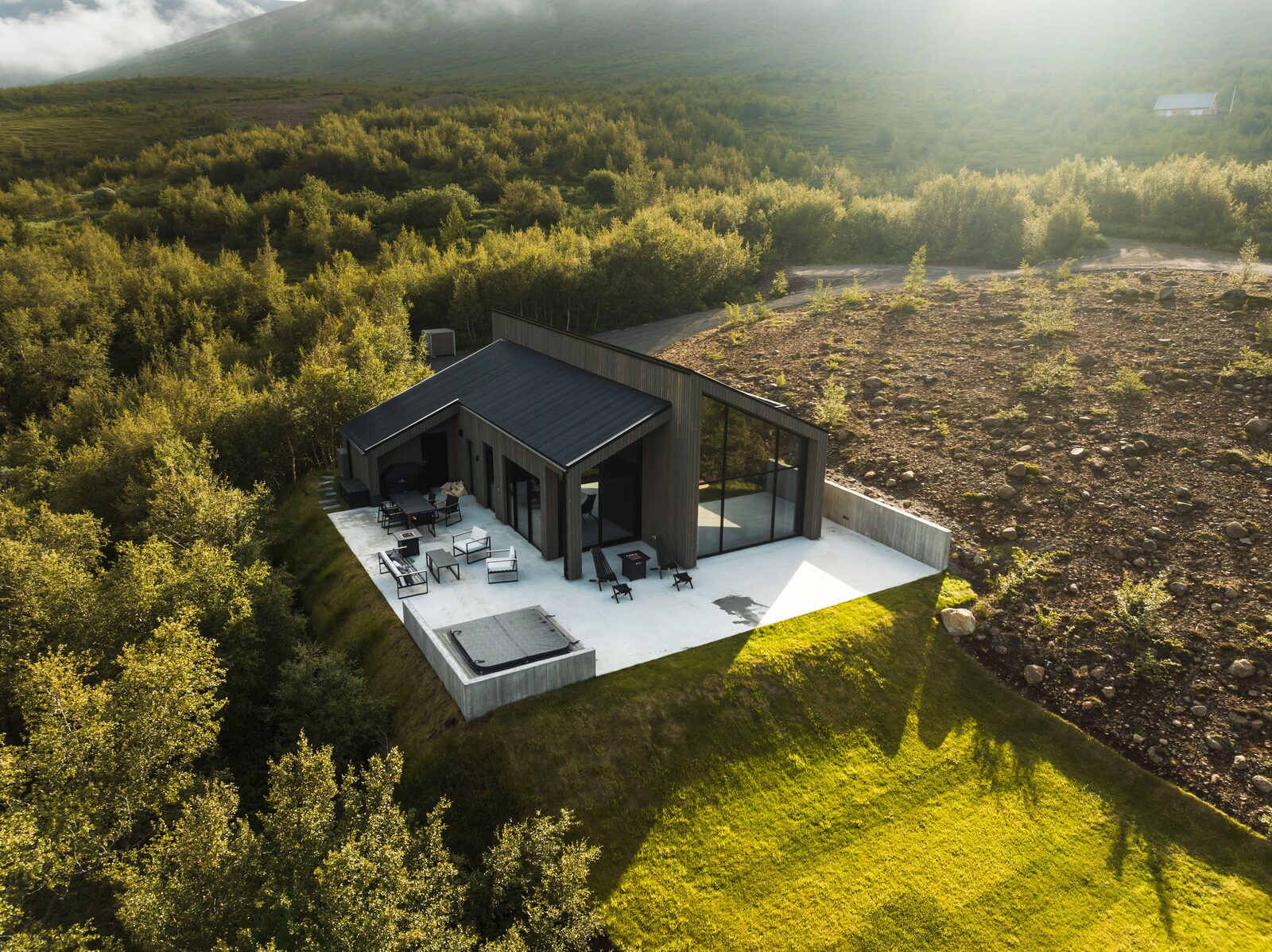 An aerial view of the house at Lundskógur among the birch trees, with the terrace and hot tub visible.