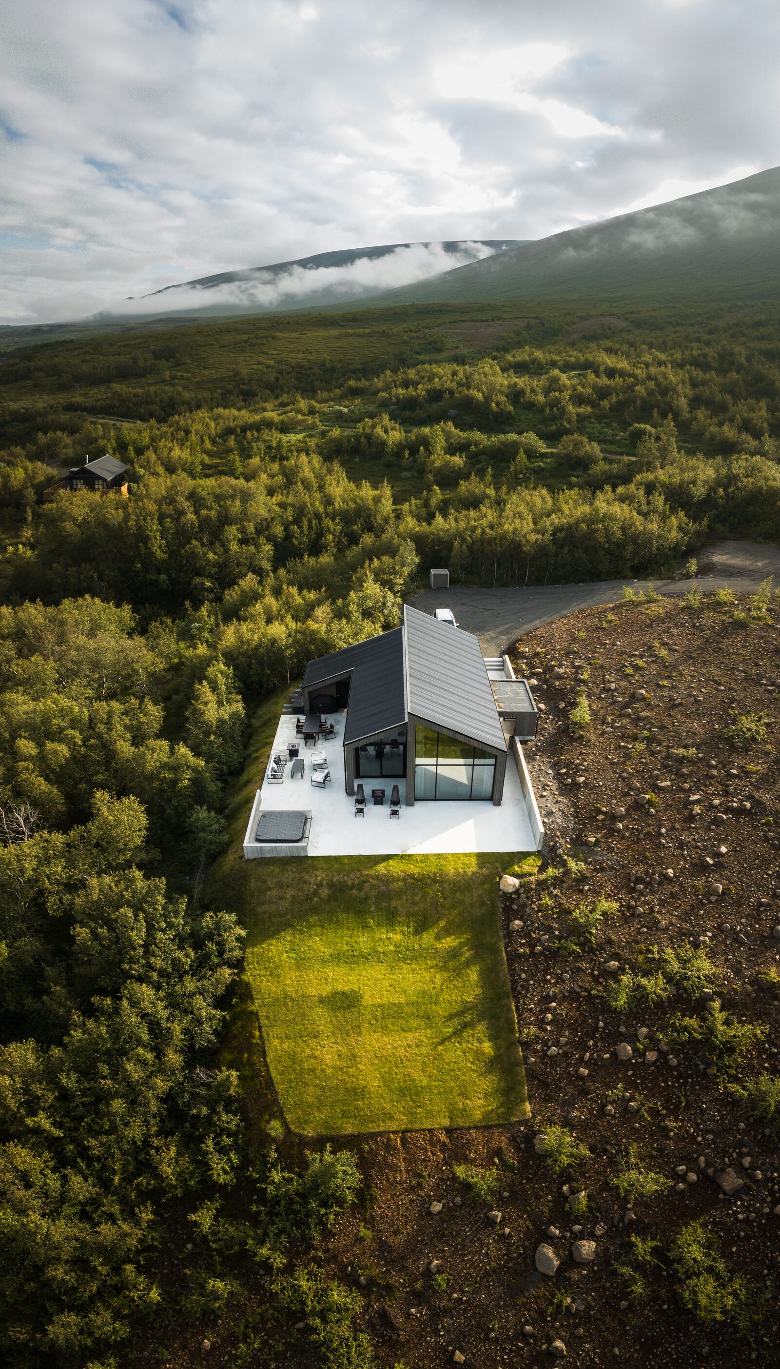 An aerial view over the green forest towards the house at Lundskógur.