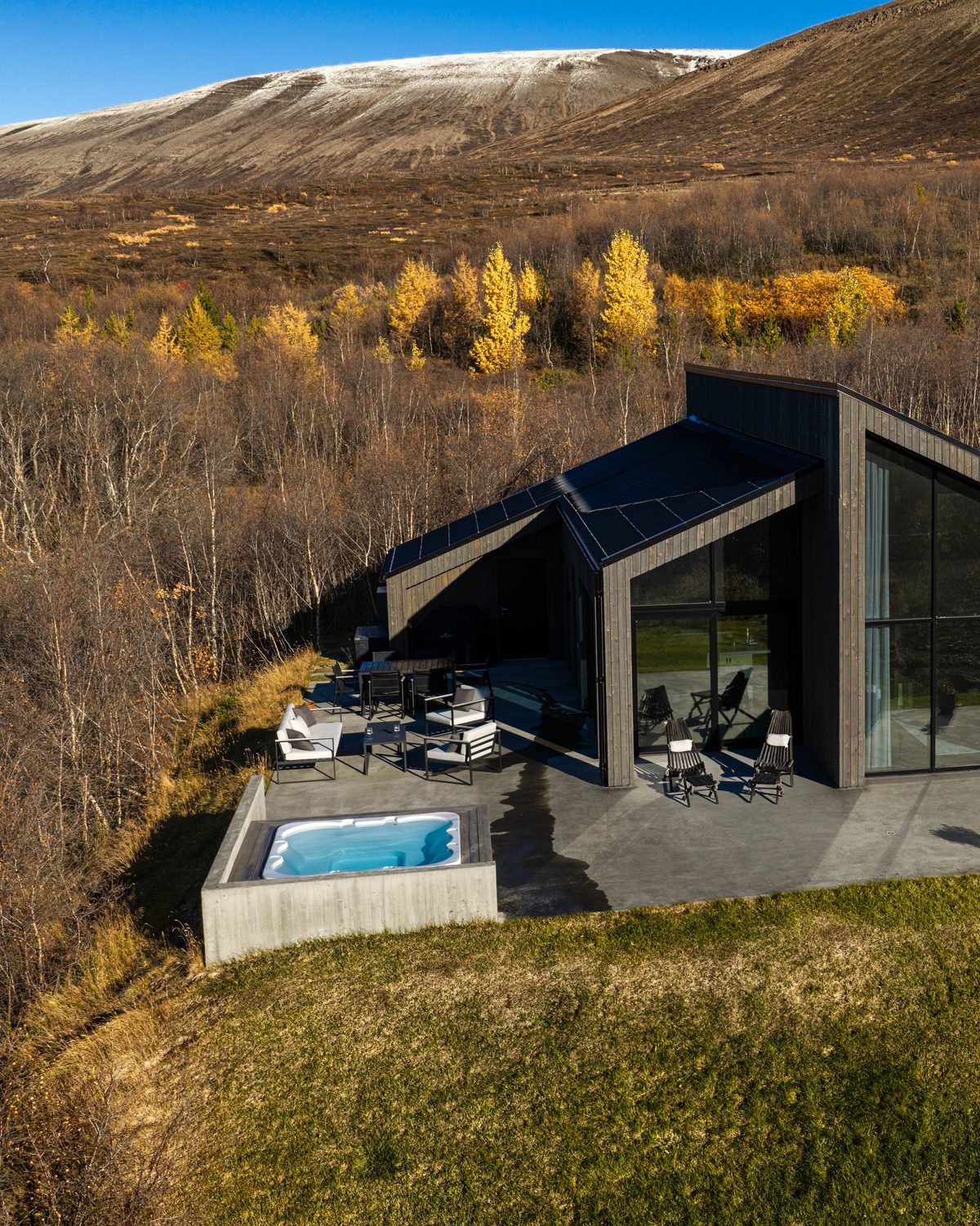 An aerial view of the terrace at Lundskógur, with the lounge seating, the hot tub and the corner of the house among autumn birch trees.