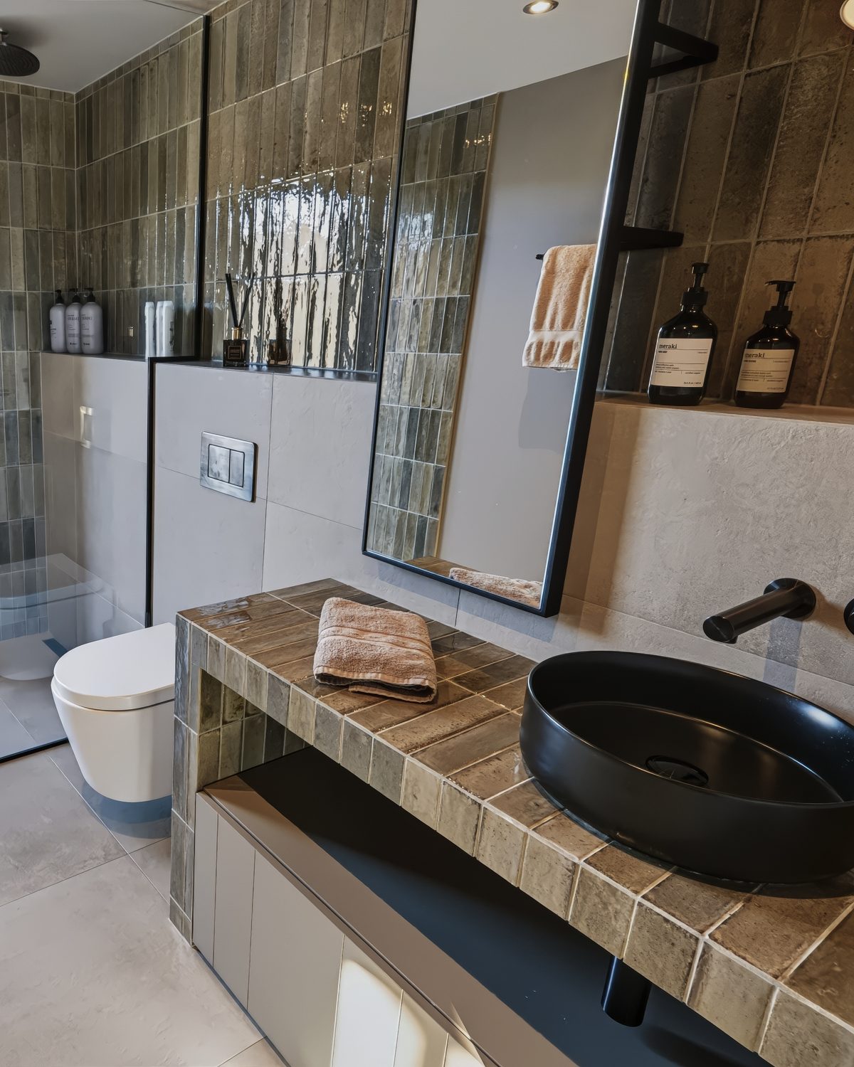 The ground-floor bathroom at Lundskógur, a black basin on a tiled vanity beside the toilet and the shower, with a tall mirror above.