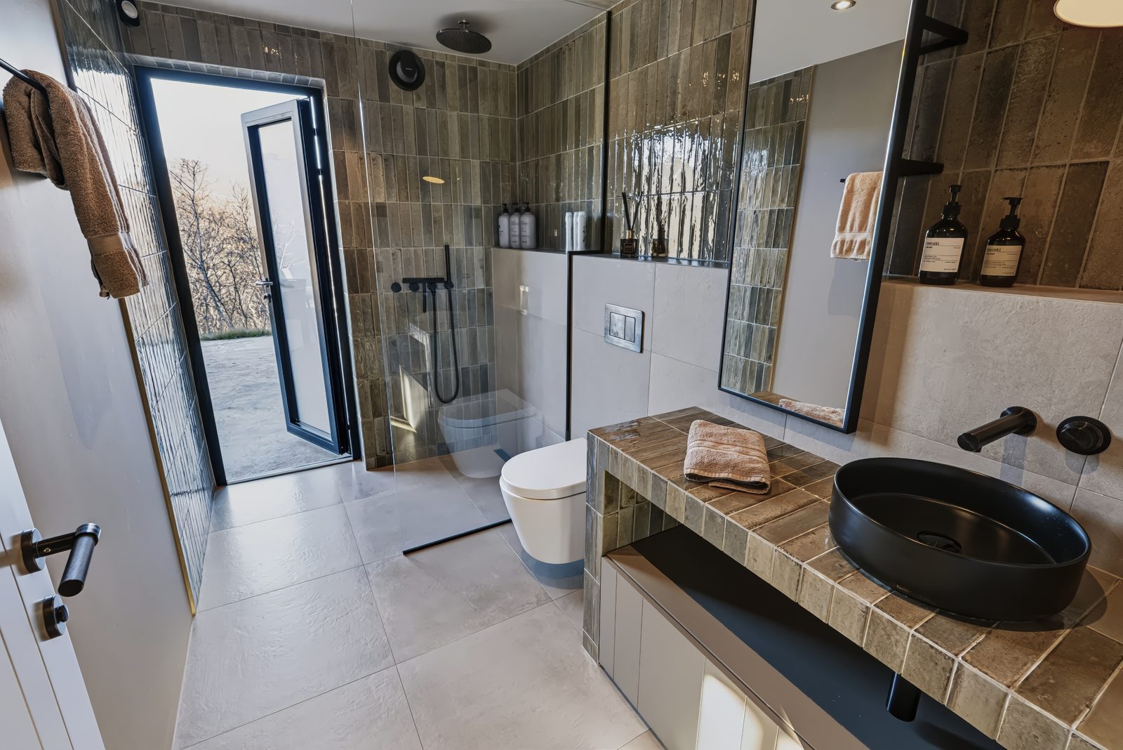 The ground-floor bathroom at Lundskógur, with the walk-in shower, the toilet, a black basin on a tiled vanity and a glass door to the terrace.