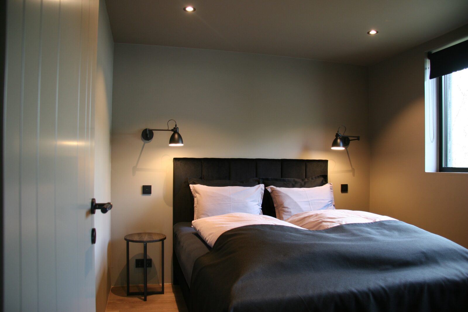 A downstairs bedroom with a queen-size bed, a dark upholstered headboard and black wall lights.