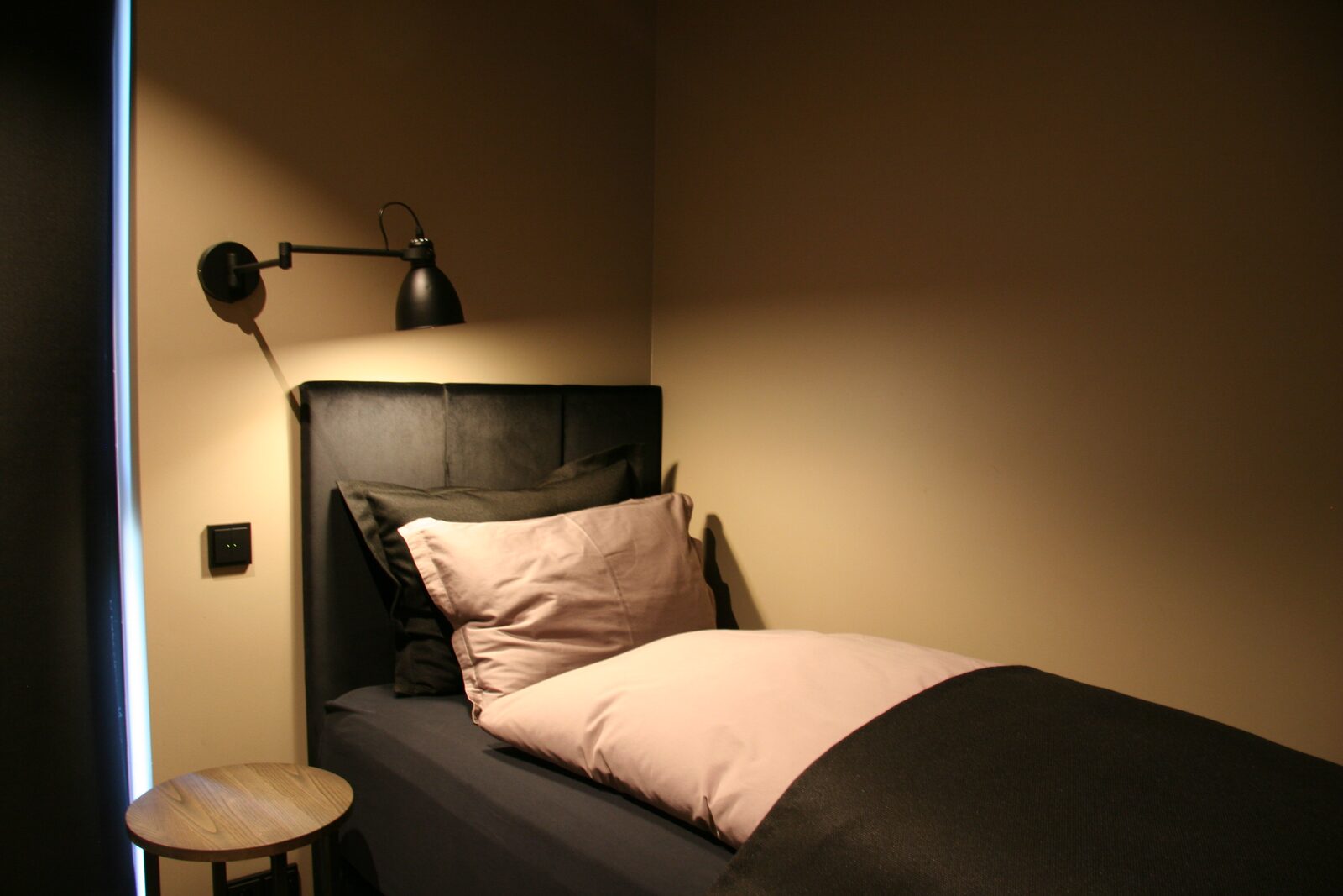 The downstairs single bedroom, with a dark bed frame and black wall light.