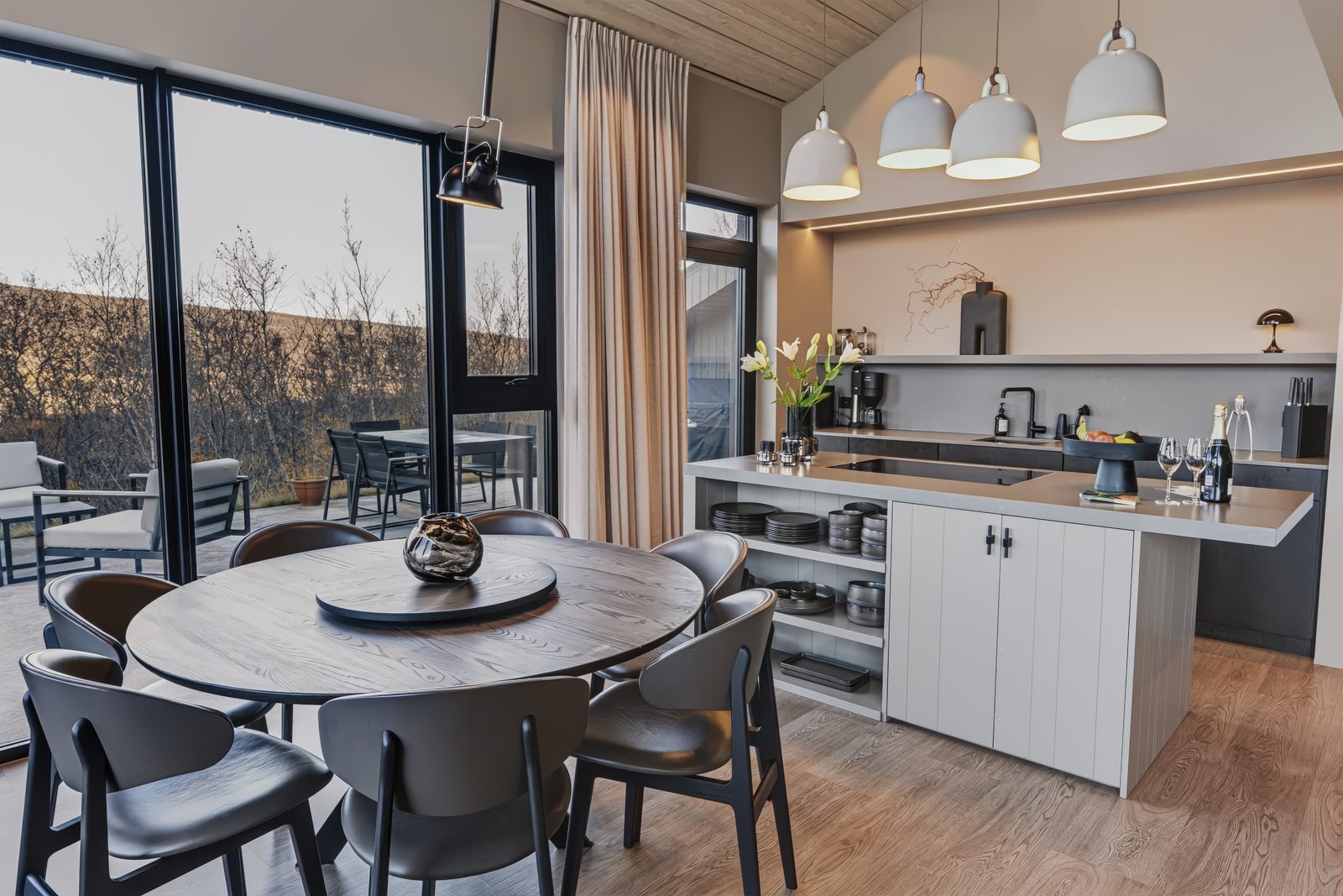 The round dining table in front of the kitchen island and the glass wall facing the terrace.