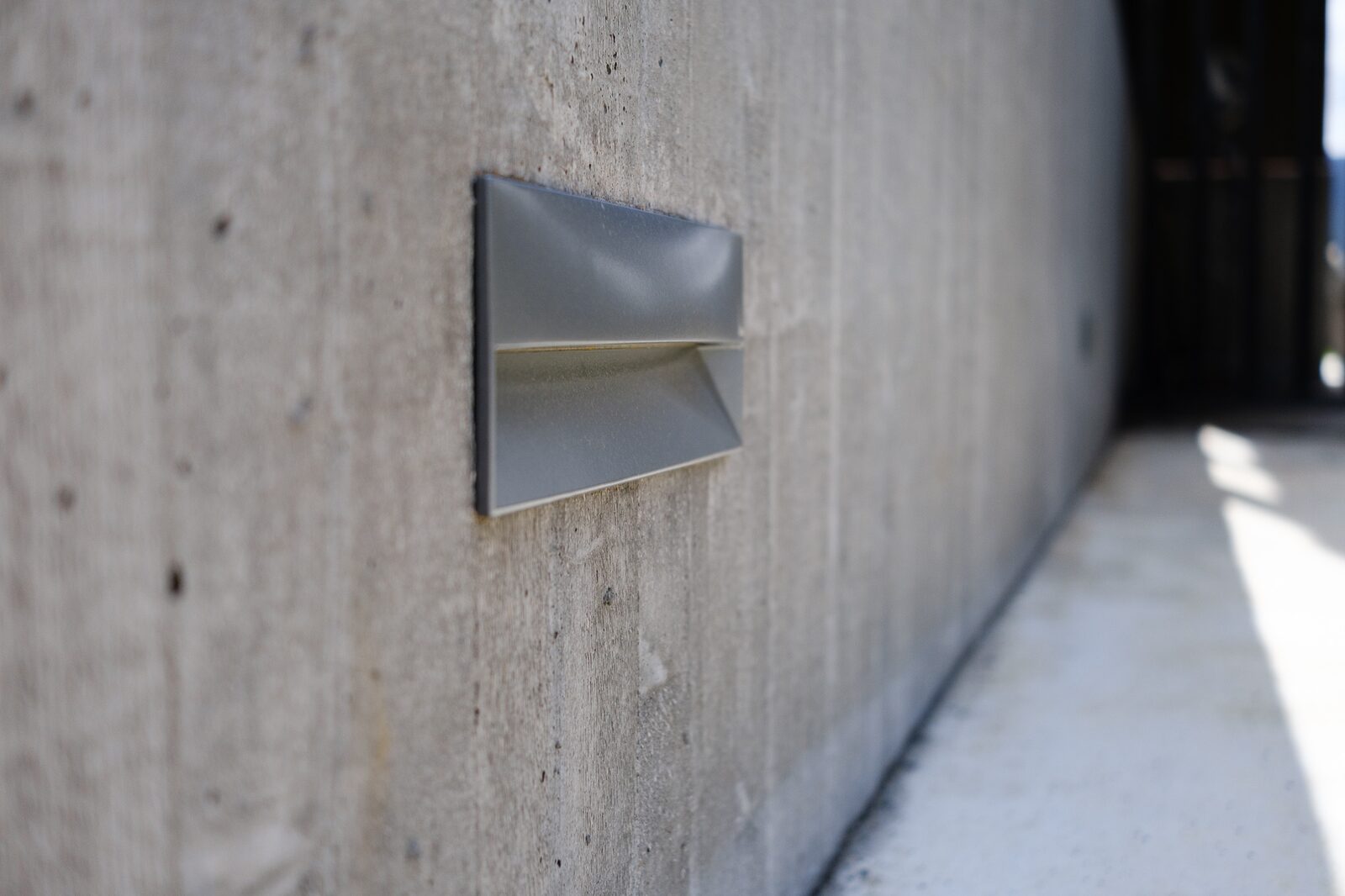 A triangular exterior light set into the concrete wall.