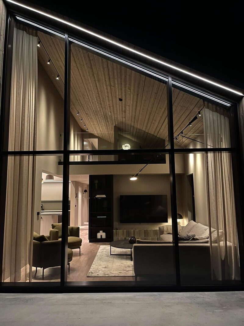 The living area glowing through the tall glass gable at Lundskógur at night.