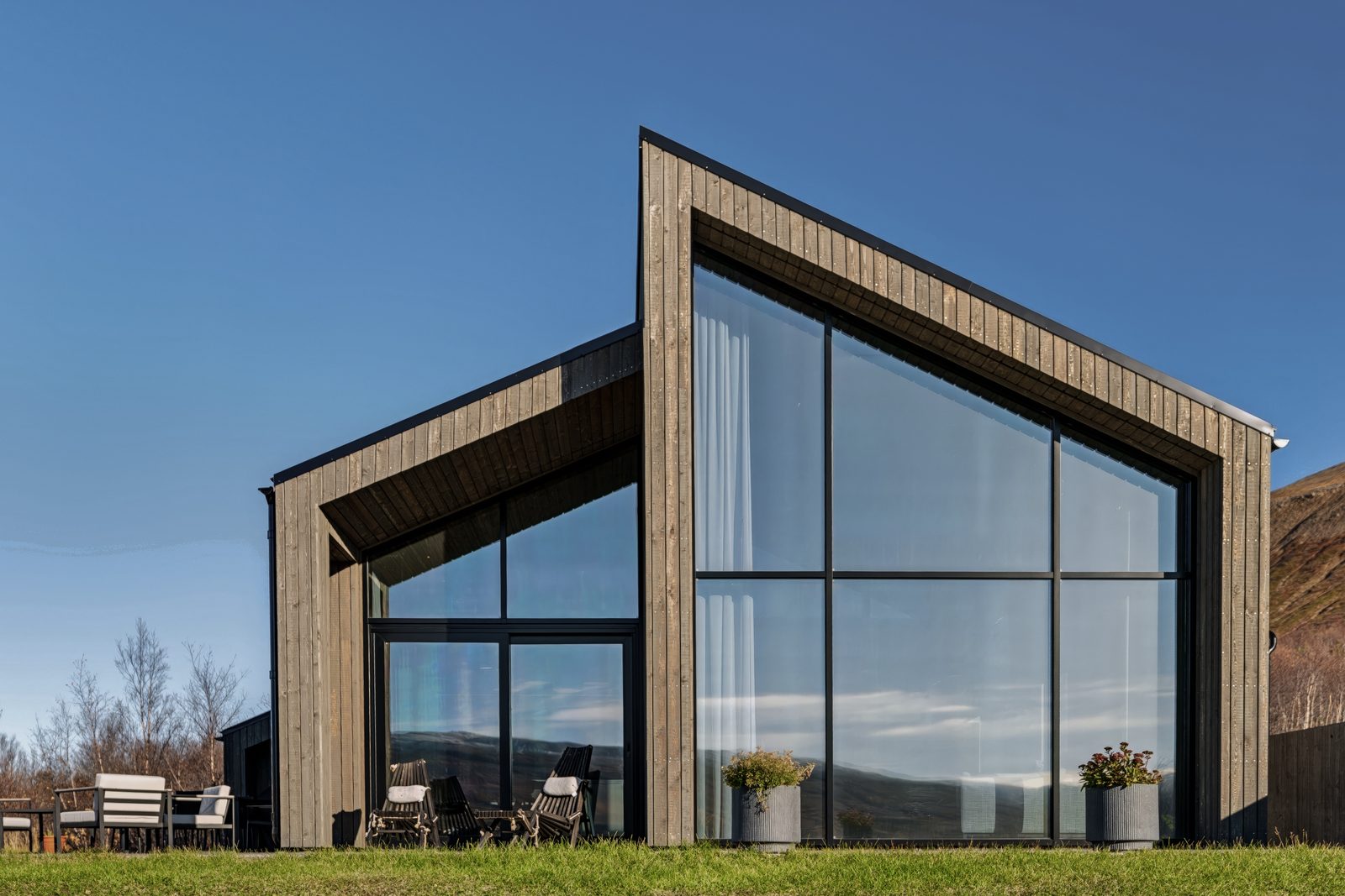 The front of the house at Lundskógur, the tall glass gable and the terrace under a clear blue sky.