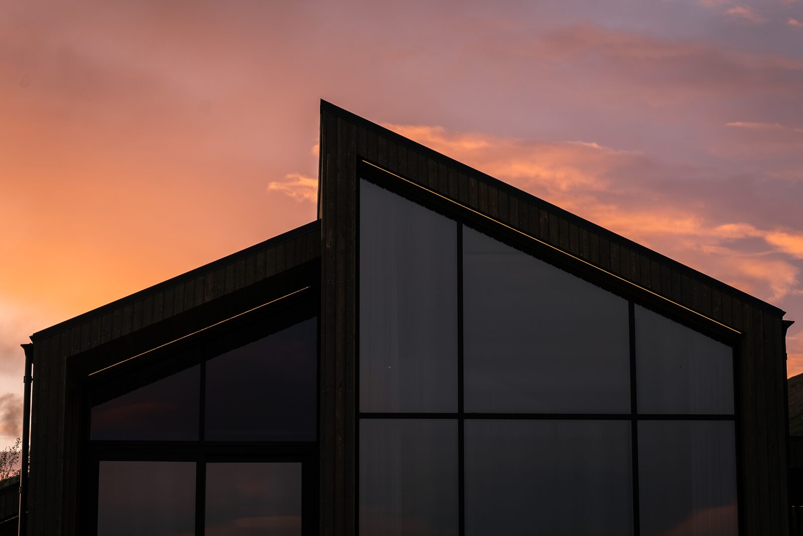 The glass gable of the house at Lundskógur silhouetted against a pink and orange sunset.