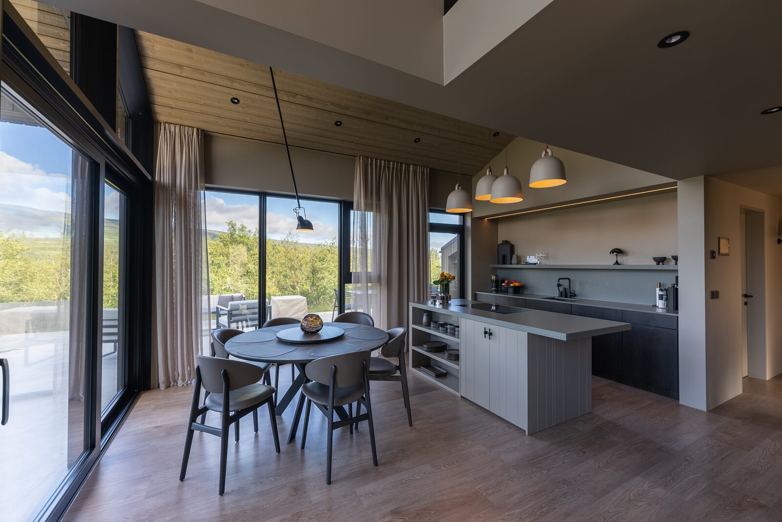 The kitchen and dining area at dusk, lit by warm pendant lights beside the windows.