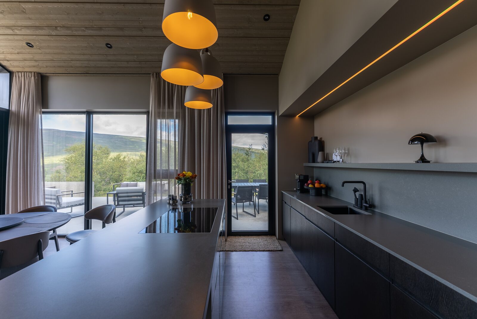 The kitchen and dining area beneath warm pendant lights, with full-height windows alongside.