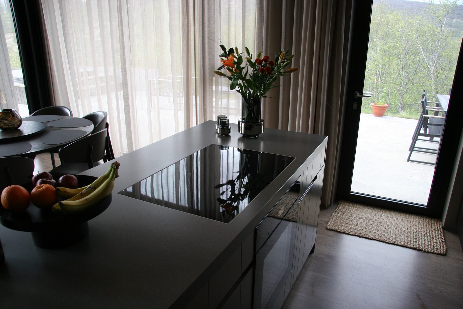 The dark kitchen island with flowers and fruit, with the entrance beyond.
