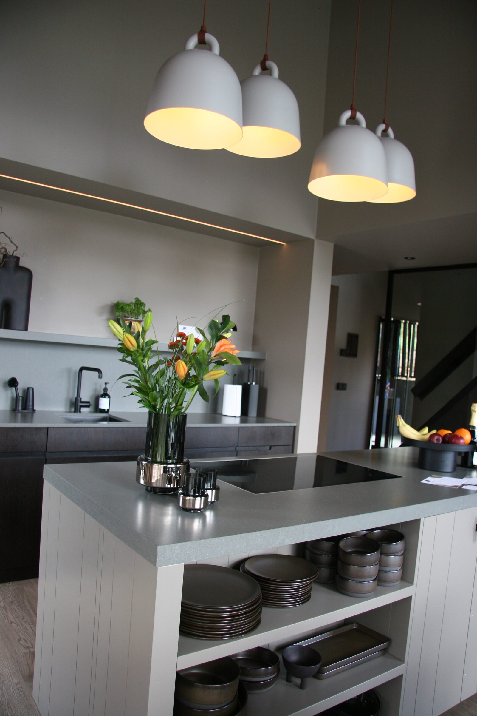 The kitchen island beneath pendant lights, with flowers and stacked crockery.