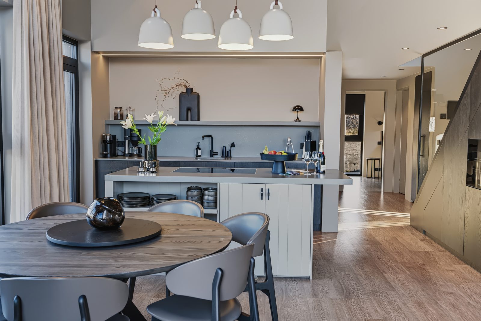 The kitchen island and shelves under four pendant lights, seen past the round dining table.