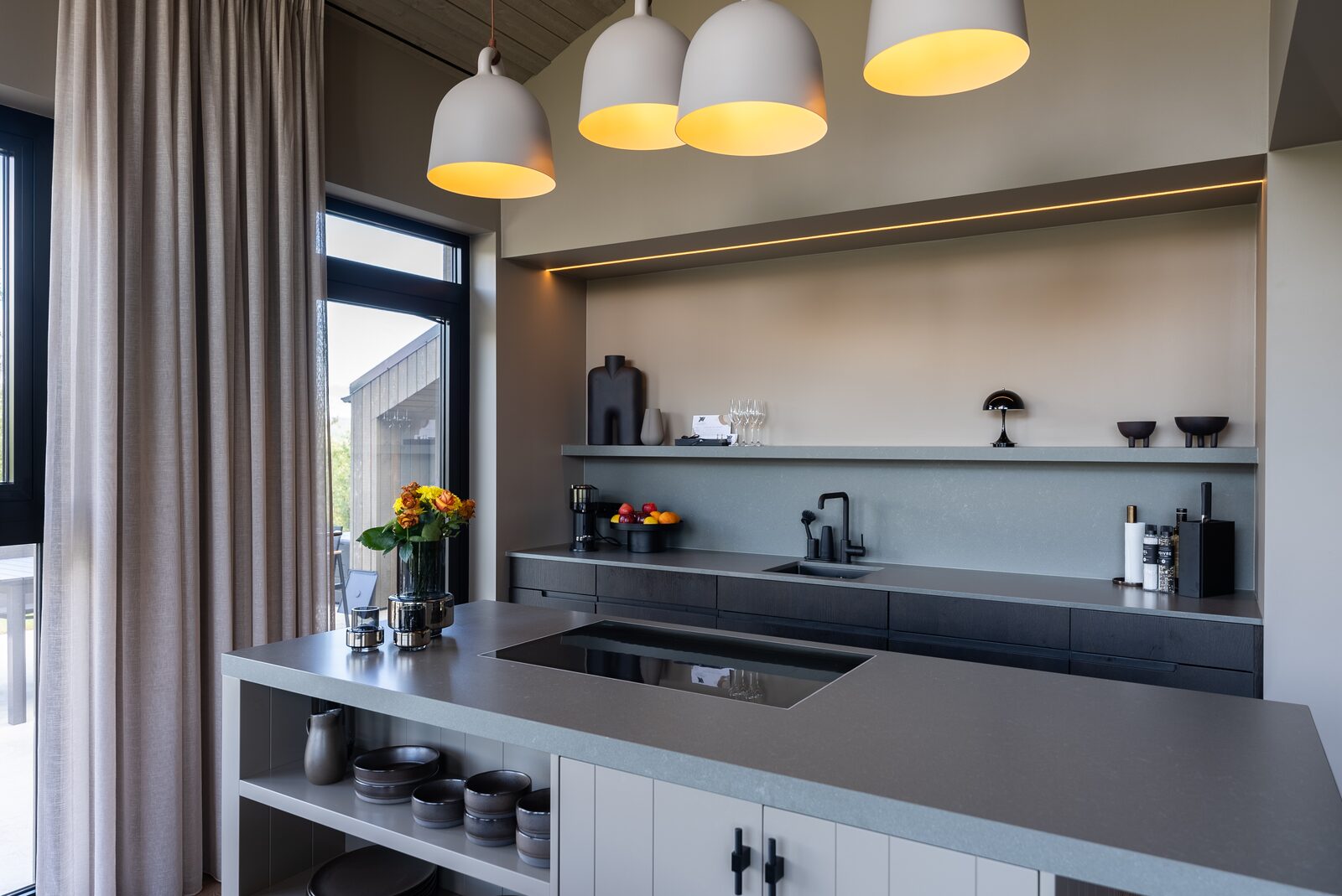 The kitchen counter at Lundskógur beneath pendant lights, with flowers and a bowl of fruit.
