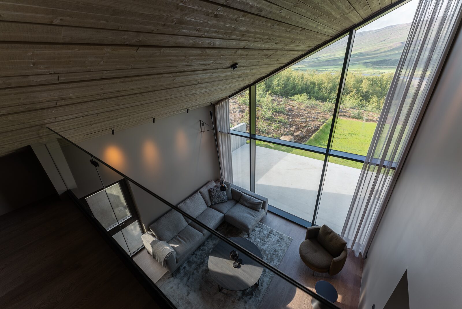 The living area seen from the upstairs landing, with full-height windows facing the valley.