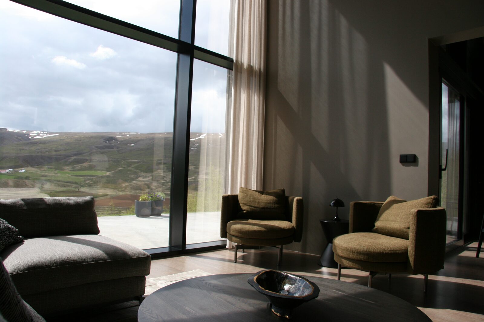 The living area at Lundskógur, with a grey sofa and armchairs facing floor-to-ceiling windows over the valley.