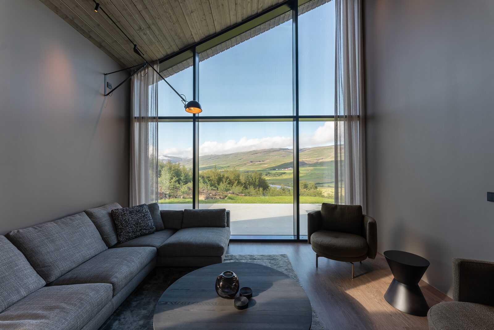 The living area sofa and side table beside sheer curtains and a full-height window.