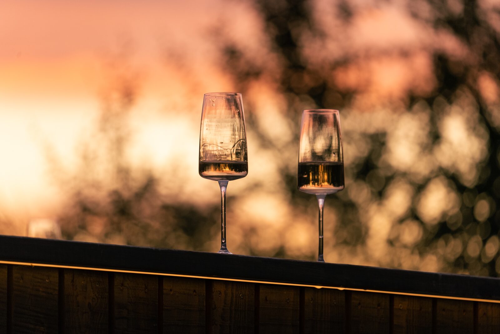 Two champagne glasses on the terrace at sunset, with birch trees behind.